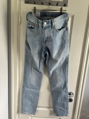 H&M Ljusblå raka jeans med hög midja - Säljer ett par ljusblå jeans med rak passform och hög midja. Klassisk femficksmodell med knapp och dragkedja framtill. Jeansen har en avslappnad look och är tillverkade i denim med en lätt tvättad finish.