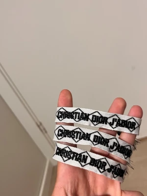 Vita hårband från Christian Dior - Tre vita hårband med svart broderad text 'Christian Dior J'Adior' och grafiskt mönster. Tillverkade i tyg med elastisk känsla, perfekta för att ge en lyxig touch till din frisyr.