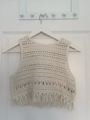 Beige croppad topp - Aldrig använd! Snygg beige linnetopp med fransar nertill. Toppen är ärmlös och har en croppad passform. 