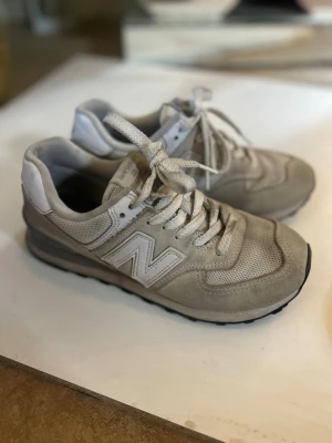 Gråa New Balance sneakers - Snygga gråa sneakers från New Balance med klassisk mesh och mocka på ovandelen. Skorna har vita detaljer, ikoniska N-loggan på sidan och vita skosnören. Yttersulan är svart och ger bra grepp. Perfekta för en avslappnad streetstyle-look.