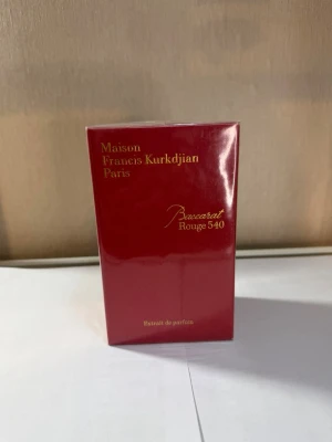 Baccarat Rouge 540 Extrait de Parfum - Maison Francis Kurkdjian Baccarat Rouge 540 Extrait de Parfum i elegant röd kartong med guldfärgad text. Lyxig och ikonisk doft från Paris, känd för sin unika och intensiva parfymblandning. Förpackningen är rektangulär och tillverkad av kartong.