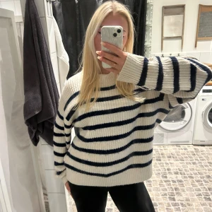 Randig stickad tröja - Mysig stickad tröja i vitt med marinblå ränder. Tröjan har en avslappnad passform och långa ärmar, perfekt för kyligare dagar. Den ribbade strukturen ger en extra touch av stil.