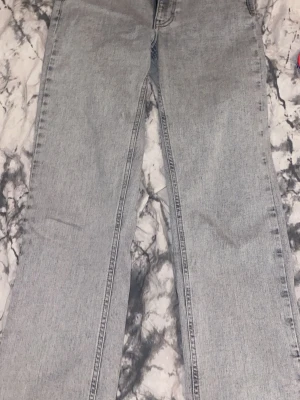 Ljusgrå raka jeans från NA-KD - Säljer ett par ljusgrå jeans från NA-KD med rak passform och klassisk femficksdesign. Jeansen har hög midja och är tillverkade i denim med en snygg tvättad look. Perfekta för en avslappnad och trendig stil.