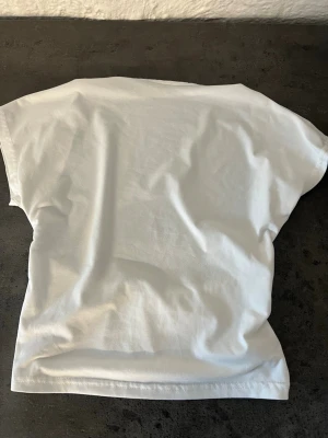 Vit kortärmad  linne  - Säljer en vit line i bomull med korta ärmar och resårdetalj i midjan på baksidan. Enkel och clean design som passar till det mesta. Perfekt för dig som gillar basic men ändå vill ha en liten twist.