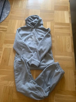 Corteiz - Säljer ett par gråa mjukisbyxor i set med en hoodie. Byxorna har resår i midjan och vid bensluten, och hoodien har dragsko och tryck framtill. Perfekt för chill dagar eller när du vill vara extra bekväm. Mjukt material som känns skönt mot huden.