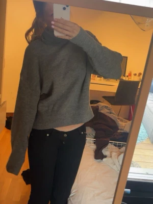 Grå polotröja i stickat material - Säljer en grå stickad polotröja med avslappnad passform och långa ärmar. Tröjan är croppad och har en hög krage som ger en cool och mysig vibe. Perfekt att matcha med jeans eller kjol för en trendig look.