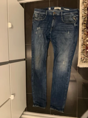  Replay jeans med slitningar - Säljer ett par mörkblå Replay jeans med slitningar i fint skick.  Riktigt snygg passform med klassisk Replay-look och slitningar som ger en modern och lite edgy stil. Perfekta till vardag och lätta att matcha med både t-shirt, hoodie eller skjorta.  Bekväma att bära och har fortfarande mycket liv kvar i sig.  Om ni vill kan jag också skicka en bild på passformen så ni ser hur de sitter på.