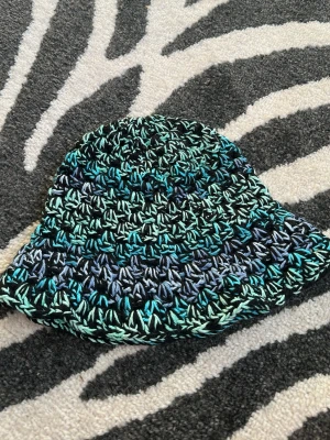 Handvirkad bucket hat i blå toner - Unik handvirkad bucket hat i svart och blåskiftande bomullsgarn  garn. Har längre volanger än de andra i min profil, sitter tajt på mitt huvud med 55cm k omkrets