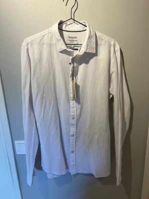 Helt oanvänd Vit linneskjorta från Jack & Jones med prislapp kvar. - Fräsch vit skjorta från Jack & Jones , tillverkad i en skön mix av bomull och linne. Skjortan har klassisk krage, knäppning framtill och långa ärmar. Perfekt för en stilren look med avslappnad känsla.                Nypris 399, mitt pris 250!