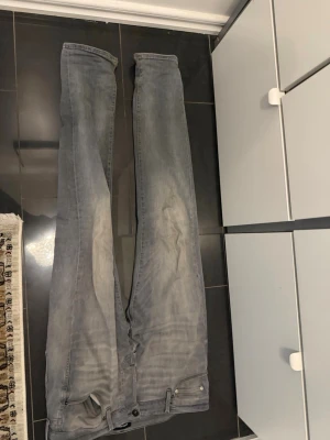 Grå slim fit jeans - Snygga grå slim fit jeans med klassisk femficksdesign och diskret slitning på låren. Jeansen har dragkedjegylf och bälteshällor. Perfekta för en avslappnad och trendig look.