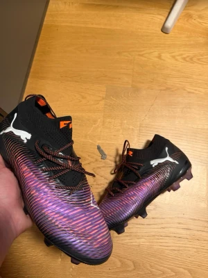Puma svarta/lila elite fotbollskor - Änvända kanske 2 gånger efter som jag slutade på fotboll kort efter jag köpte dem. Säljer ett par snygga fotbollsskor från Puma i svart och lila med vita detaljer. Skorna har en strumpliknande passform, snörning och mönstrad ovandel för bättre bollkontroll. Perfekta för spel på gräsplaner och har klassisk Puma-logga på sidan.