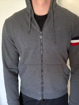 Moncler Zip hoodie  - Snygg grå moncler hoodie (gammal model). Praktiska fickor framtill och ribbade muddar. Perfekt för en avslappnad stil.