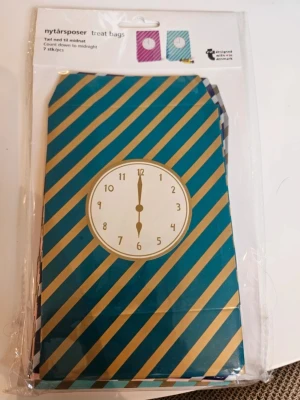 Nytårspåsar med klockmotiv 7-pack - Säljer ett paket med 7 stycken treat bags för nyår, dekorerade med diagonala ränder och en klocka som visar midnatt. Påsarna är i färgerna blått och lila med guldiga detaljer. Perfekta för godis eller små överraskningar till nyårsfirandet.