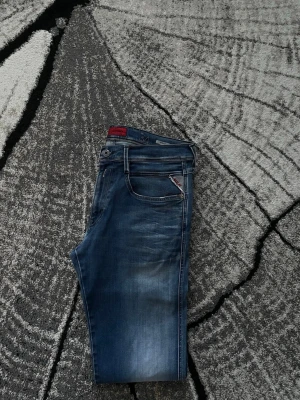 Replay anbass jeans - Snygga blå slim fit jeans från replay med klassisk femficksdesign och diskreta slitningar. Jeansen har röda detaljer vid fickan och en röd etikett i linningen. Tillverkade i denim med stretch för extra komfort. Byxorna är i Hyperflex vilket gör de mycket skönare. Nypris 1699kr | mitt pris 649 | byxorna är i 9/10 skick knappt använda w33 L 34