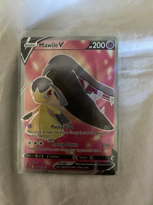 Pokémonkort Mawile V holo - Säljer ett Pokémonkort Mawile V med holografisk yta. Kortet har färger i rosa, svart och gult och är från Sword & Shield-serien. Det är en basic V-kort med 200 HP och coola attacker som Pouty Slap och Chomp Down.