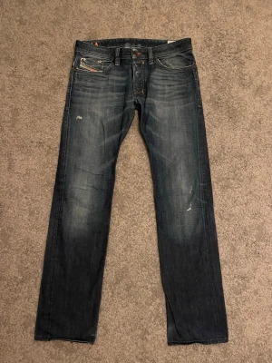 Regular slim-straight Diesel Safado - Snygga mörkblå jeans från Diesel av modell "SAFADO" med slitna detaljer. Jeansens passform är "Regular slim-straight", strl W32 L34. Orangea sömmar. Tillverkade i denim med en mörk wash (008Y3)..