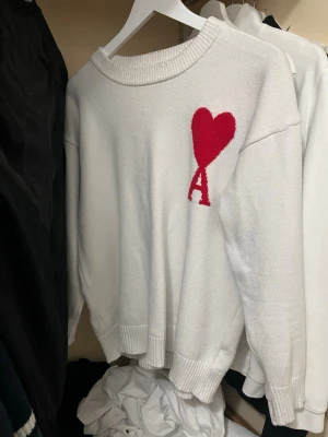Ami Paris stickad tröja - Vit stickad tröja från AMI Paris. Tröjan har rund halsringning och ribbade muddar. Perfekt för dig som gillar stilrena plagg med en twist. Storlek M men rekommenderar för den som har S då den blivit mindre pågrund av några tvätt