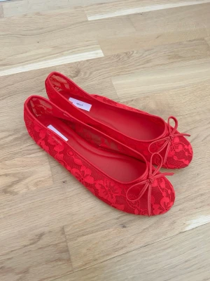 Röda spetsballerinas från Nelly - Snygga röda ballerinaskor från Nelly med spetsdetaljer och rosett framtill. Skorna har rund tå och är täckta med blommig spets som ger en trendig och feminin look. Perfekta för att lyfta vilken outfit som helst. Aldrig använda 