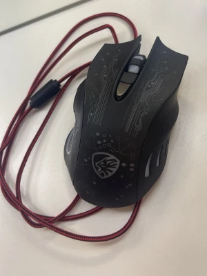 Svart gamingmus från Bloody - Säljer en svart gamingmus från Bloody med mönster av kretskort och logga på ovansidan.Musen lyder även flera olika färger när man har kablat in den. Musen har flera knappar, röd tygklädd USB-kabel och ergonomisk form för gaming. Sladen är ungefär 1meter och 46cm. Perfekt för dig som vill ha snabb respons och cool design till datorn.