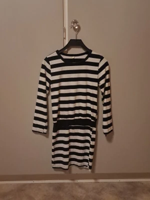 Randig svartvit klänning - Säljer en svartvit topp/klänning med breda horisontella ränder och trekvarts ärmar. Klänningen har rund halsringning och är i mjukt, stretchigt material. Perfekt för dig som gillar en enkel men snygg stil. I stil 2000s / early 2010s vintage. Den är storlek 150 o skulle säga att det motsvarar 32 o passar en som är XXS/XS 