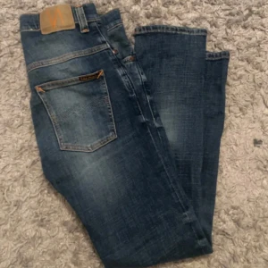 Nudie Jeans  - Säljer ett par blå slim fit jeans från Nudie Jeans i storlek 29/30. Jeansen har klassisk femficksdesign, snygga slitningar och orangea sömmar. Materialet är mjukt denim i bomull och passformen är smal och modern.  Dom är i väldigt bra skick förutom några mindre hål mellan benen men det går att fixa helt gratis hos nudies butiker. Det är bara skriva om du undrar något! Pris kan diskuteras vid en snabb och smidig affär 