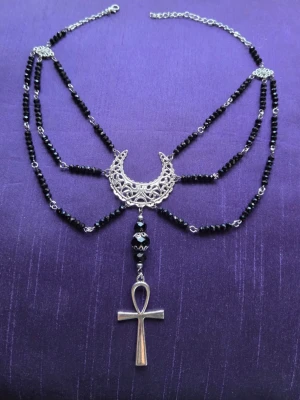 Svart gotiskt halsband med ankh och måne goth bohem moon  - Unikt halsband med svarta pärlor, silverfärgad kedja och detaljer. Smycket har en stor dekorativ halvmåne i metall och ett hängande ankh-kors. Perfekt för dig som gillar alternativ stil och statement-accessoarer. Egendesignat/egenkomponerat.