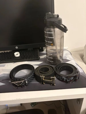 Tre svarta bälten med metallspännen - Tre snygga svarta bälten med olika metallspännen. Ett har ett rutmönster och X-formad detalj, ett ha Hermens  och det tredje har textdetaljer på remmen. Perfekta accessoarer för att lyfta din outfit.