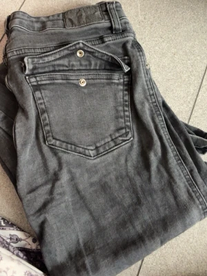 Grå jeans med raka ben - Snygga grå jeans med raka ben och klassiska bakfickor med knappdetaljer. Jeansen har en avslappnad passform och är tillverkade i mjukt denimtyg. Perfekta för en cool och avslappnad stil.
