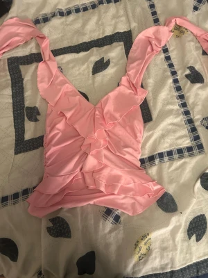 Rosa volangbikini från SHEIN - Supersöt rosa bikiniöverdel från SHEIN med volangdetaljer och breda axelband. Bikinin har en omlottkänsla framtill och är gjord i mjukt syntetmaterial som känns bekvämt mot huden. Perfekt för strandhäng eller poolparty!