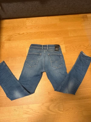 Blå grover slim jeans från replay  - Säljer ett par klassiska blå jeans från Jack & Jones med slim ben och femficksmodell. Jeansen har snygga slitningar framtill och en mörkare tvätt baktill. Tillverkade i bomull med lite stretch för extra komfort. Perfekta för en avslappnad och trendig look.