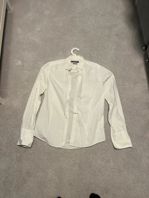Vit skjorta från Tiger of Sweden - Klassisk vit skjorta från Tiger of Sweden i slim fit-modell. Skjortan har långa ärmar, knappar framtill och en stilren krage. Perfekt för dig som gillar en clean och tidlös look.