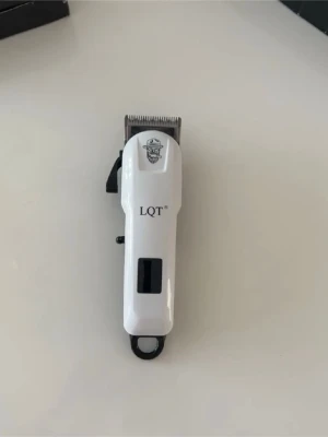 LQT hårtrimmer med tillbehör - Elektrisk hårtrimmer från LQT i vit plast med svart detalj och metallblad. Medföljer flera svarta plastkammar i olika längder för varierad klippning. Perfekt för att fixa frisyren hemma och enkel att använda tack vare ergonomiskt handtag.