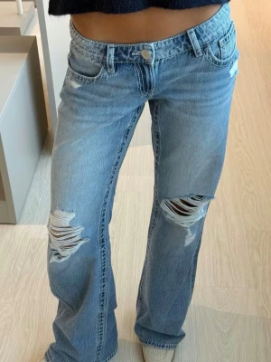 Lågmidjade jeans - Snygga lågmidjade ljusblå bootcut jeans med slitningar och hål på båda knäna. Dem är ifrån Gina Young 14+ i storlek M och den slutsålda modellen ”for real low loose jeans! Skulle säga att dem passar dig som har M/L i vanlig storlek! Endast andvända 1 gång! 