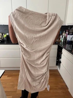 Beige omlottklänning från Boohoo - Säljer en beige omlottklänning från Boohoo i storlek 36. Klänningen har en draperad design med snygga rynkdetaljer längs sidan och är tillverkad i ett mjukt material. Perfekt för dig som gillar en stilren och trendig look.