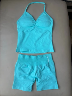 Turkost set från DFINE med topp och shorts - Säljer ett turkost set från DFINE med en halterneck topp och matchande shorts. Topp med lätt vaddering och rynkdetalj vid bysten, shorts med bred resår i midjan. Mjukt och stretchigt material, perfekt för en sportig look.