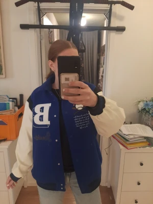Baseball/bomberjacka - Storlek M. Snygg bomberjacka i college-stil med blå kropp och vita ärmar. Stort vit B på bröstet, broderad text och basebollmotiv. Köpt från H&M för ca 450kr.