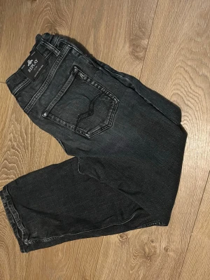 Svarta Replay jeans med raka ben - Säljer ett par svarta jeans från Replay med klassisk femficksdesign och raka ben. Jeansen har en snygg tvättad look och detaljerade sömmar på bakfickorna. Perfekta för dig som gillar en avslappnad men stilren vibe.