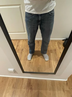 Blå jeans från GANT med raka ben - Säljer ett par klassiska blå jeans från GANT med raka ben och femficksdesign. Jeansen har en snygg ljusblå tvätt med subtila slitningar och GANT-logga på myntfickan. Materialet är denim i bomull och passformen är avslappnad. Storlek 34/30 men är justerade längst ner så mer 32/30