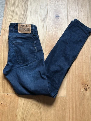 Mörkblå slim jeans från Replay - Snygga mörkblå jeans från Replay med slim fit passform. Klassisk femficksmodell med Replay-logga på myntfickan och läderpatch bak i midjan. Jeansen är gjorda i stretchigt denimtyg som ger en bekväm känsla och sitter snyggt HELT NYA