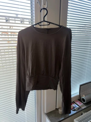 Mörkbrun croppad sweatshirt, Gina Tricot - En enkel och stilren mörkbrun croppad sweatshirt med rund halsringning och långa ärmar. Tröjan har en bred mudd vid midjan och är tillverkad i ett mjukt, stretchigt material som passar perfekt till jeans eller kjol.