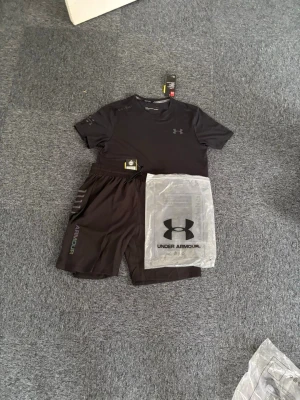   Under Armour träningsset - Snyggt svart träningsset från Under Armour med t-shirt och shorts. Setet har diskreta loggor på både tröjan och shortsen. Tillverkat i ett lätt och snabbtorkande material som passar perfekt för träning och sportaktiviteter. L passar M