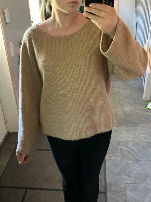 Beige oversized stickad tröja - Mysig beige stickad tröja med avslappnad passform och bred halsringning. Tröjan har långa, vida ärmar och är tillverkad i ett mjukt, ribbstickat material. Perfekt för lager-på-lager och chill dagar.