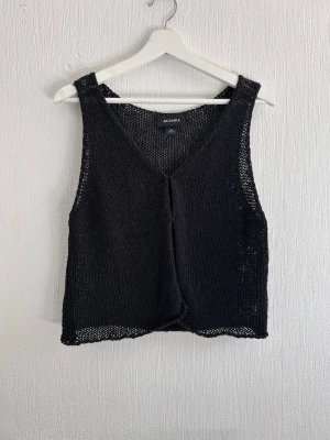 Svart stickad väst från Monki - Svart stickad väst från Monki med v-ringad hals och öppen front. Västen har en loose passform och är perfekt att slänga över en t-shirt eller klänning för en chill och trendig look.