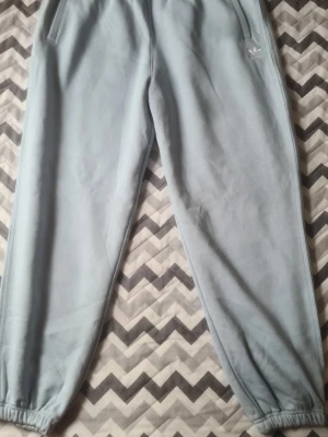 Adidas Originals Joggers – ljusblå (XL) - Adidas Originals Joggers – ljusblå (XL) Säljer ett par riktigt snygga och bekväma joggers från Adidas Originals. • Storlek: XL • Färg: Ljusblå • Modell: Jogger FL (JY3940) • Skick: Oanvänt • Mjukt och skönt material • Resår i midja och benslut • Sidofickor