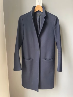 Marinblå klassisk kappa från COS - Stilren mörkblå kappa från COS som jag har svårt att släppa men den har tyvärr blivit för liten och använts alldeles för lite. Tidlös och klart värdig ett nytt hem! 