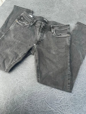 Mörkgråa jeans från Jack and Jones  - Säljer ett par mörkgrå jeans med klassisk femficksmodell och dragkedjegylf. Jeansen har en smal passform och är tillverkade i stretchigt denimtyg för extra komfort. Perfekta till en avslappnad streetstyle-look. Modell slim Glenn storlek W32 L32