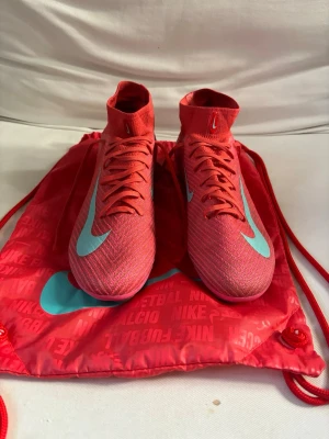 Nike Mercurial rosa fotbollsskor - Säljer ett par Nike Mercurial fotbollsskor i en riktigt snygg rosa färg med turkosa detaljer och Nike-logga. Skorna har strumpliknande skaft och en lätt, ventilerande ovandel i syntetmaterial. Sulan har aggressivt mönster för grymt grepp på planen. Perfekt för dig som vill sticka ut! Har bara haft dem i 2 månader säljer för att dem är försmå 