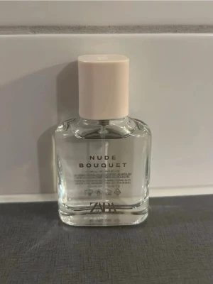 Zara Nude Bouquet parfym 30 ml - Fräsch parfym från Zara i doften Nude Bouquet. Flaskan är genomskinlig med en ljusbeige, nästan nude-färgad kork och minimalistisk design. Perfekt för dig som gillar blommiga och lätta dofter. Flaskan rymmer 30 ml och har en stilren, modern look.