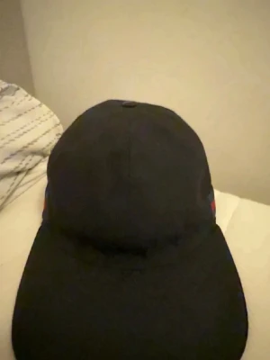 Svart keps från Gucci  - Säljer en svart keps från Gucci med klassisk böjd skärm och den ikoniska röd-gröna randen på sidan. Kepsen har en stilren design och passar perfekt till streetwear eller för att lyfta din outfit med en lyxig touch.