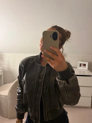 Svart bomberjacka från Zara - Snygg svart bomberjacka från Zara i ett glansigt material som ger en cool look. Jackan har ribbade muddar vid ärmslut och midja, dragkedja framtill och fickor med dragkedja. Perfekt för dig som vill ha en trendig och stilren jacka till hösten.